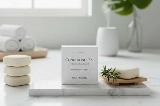 Bath products including a conditioner bar, towels on a marble surface with a plant in the background.