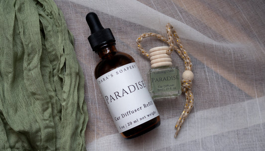 Two bottles of 'Paradise' car diffusers by Dara's Soapery on a textured fabric background.